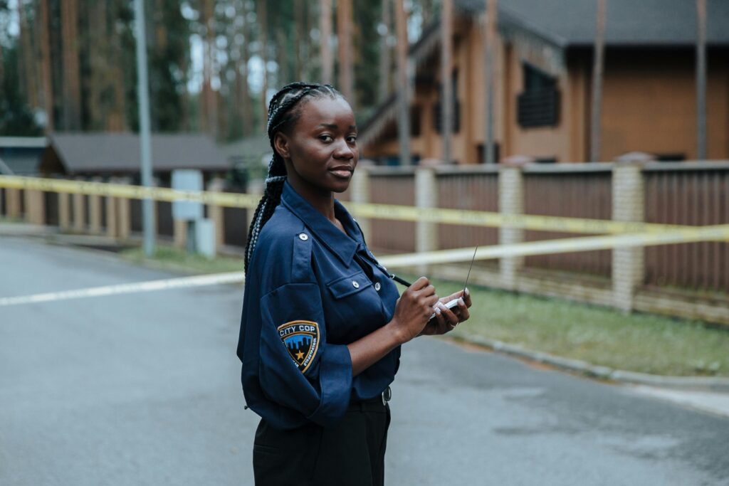 A female police officer standing outdoors near caution tape and concrete buildings during the day.