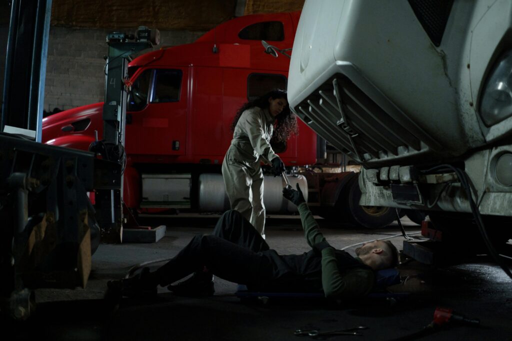 Two mechanics working together to repair a truck in a dimly lit garage setting.